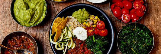 Bowl of food with rice and vegetables. Other bowls with guacamole, tomatoes, and kale next to it.