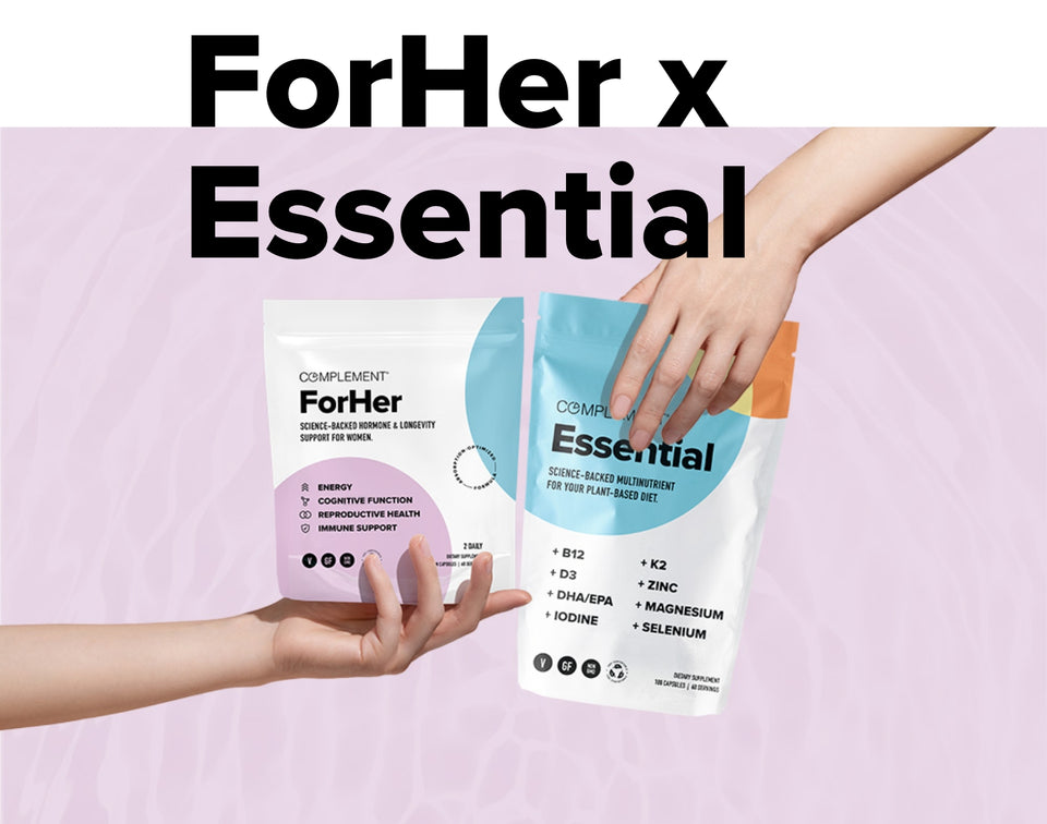 Two hands are holding packets of Complement ForHer and Essential supplements against a pastel pink background. The top text reads ForHer x Essential.