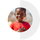 A smiling child in a red shirt stands outdoors on a sunny day, with a blurred natural background.