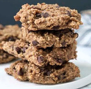 A stack of four homemade cookies with a rustic appearance, featuring visible chocolate chips. They are set on a white plate against a dark background, creating a cozy and inviting look.