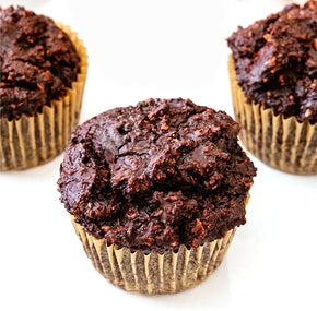 Three chocolate muffins with textured tops are arranged on a light surface. The muffins are in golden paper liners, showcasing a rich, dark chocolate hue.