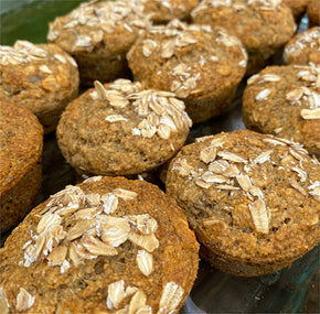 Close-up of several oat-topped muffins, freshly baked and arranged in rows. The muffins have a golden-brown color and are sprinkled with rolled oats, highlighting their rustic and wholesome appearance.