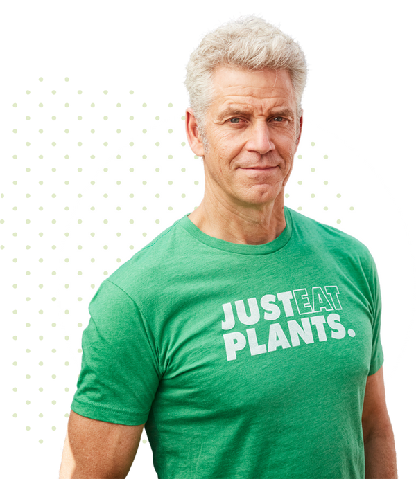 Man wearing a green T-shirt with the text JUST EAT PLANTS. stands against a graphic background of green dots and a white circle. He has short gray hair and a confident expression.