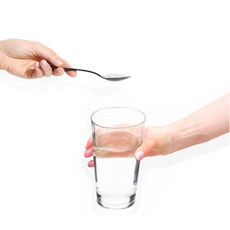 A hand on the left holds a teaspoon with a substance near a glass of water held by another hand on the right. The background is plain white.