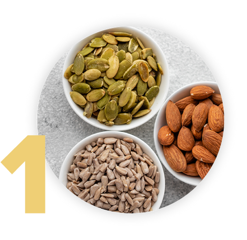 Three bowls filled with seeds and nuts. The top bowl contains pumpkin seeds, the right bowl has almonds, and the bottom bowl holds sunflower seeds. A large number 1 is visible on the left side.