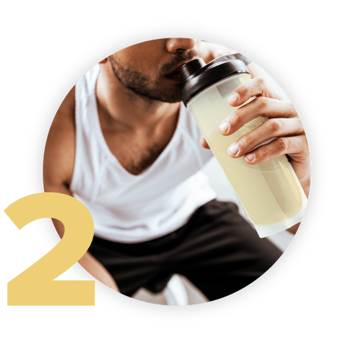 A person wearing a white tank top drinks from a shaker bottle containing a yellow beverage. The number 2 is displayed prominently in the bottom left corner of the image.