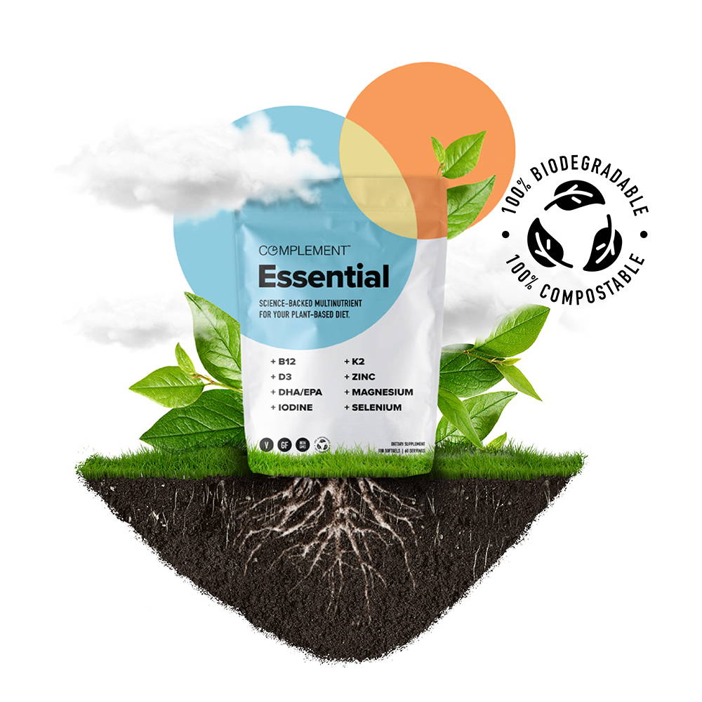 A package of Complement Essential multivitamins is shown with green leaves and soil surrounding it. A cloud is above, and a compostable symbol is visible on the right, highlighting the products eco-friendly packaging.