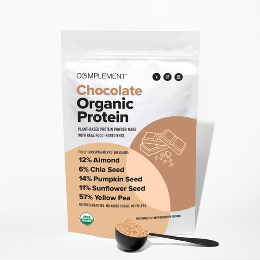 A bag of Complement Chocolate Organic Protein powder stands upright, featuring ingredient percentages and chocolate illustrations, with a scoop of the powdered supplement placed in front on a white surface.