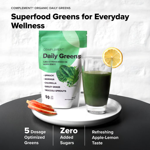 A bag of COMPLEMENT® Energy Stack by Complement stands next to a glass of green drink with a lemon slice. Apple slices are on the plate. Text highlights Superfood Greens, key ingredients, and benefits like zero added sugars.
