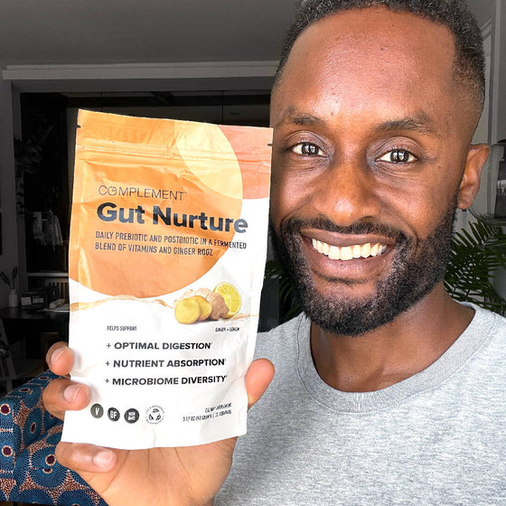 A man smiling and holding a package of Gut Nurture supplement, which promotes optimal digestion, nutrient absorption, and microbiome diversity. The packaging features images of lemons and ginger.