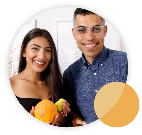 A smiling woman and man stand side by side, holding an orange and a pear. The woman has long dark hair and wears a black top, while the man wears glasses and a blue shirt. A colored circle design is in the bottom right corner.