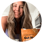 Woman with long hair smiling at the camera in a kitchen, with a package labeled Gut N... partially visible in the foreground.
