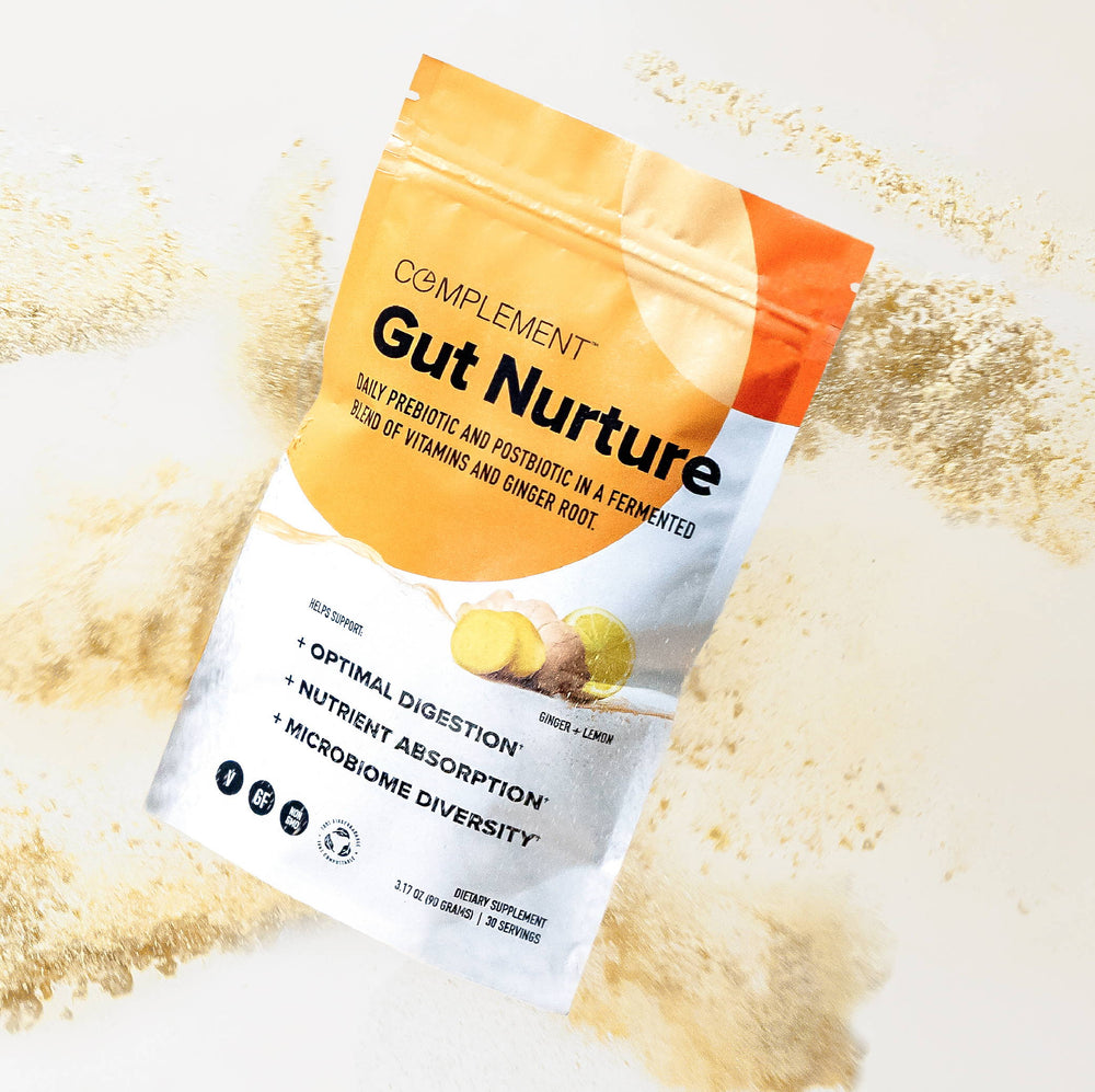 A pouch of Gut Nurture by Complement on a light surface covered with its powder. The packaging highlights features like prebiotic and postbiotic content, nutrient absorption, and microbiome diversity.