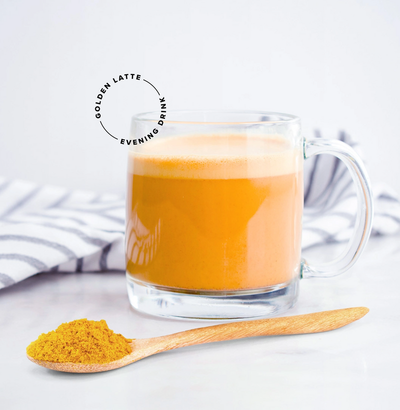 A clear glass mug filled with a golden yellow latte sits on a white surface next to a wooden spoon holding turmeric powder; a striped cloth is in the background. Text reads “Golden Latte Evening Drink.”.