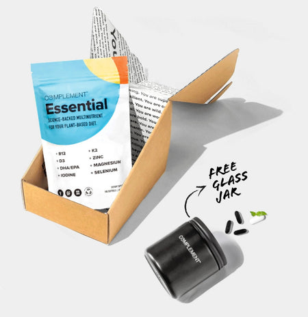 A cardboard box contains a pouch labeled Complement Essential and a black glass jar. The pouch advertises a plant-based multinutrient with vitamins and minerals. Three capsules and two leaves are displayed beside the jar with the text Free Glass Jar.