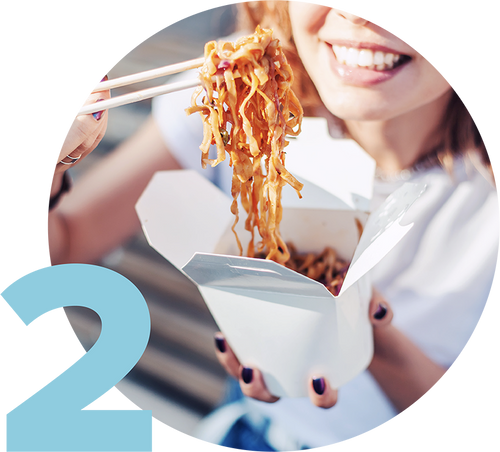 A person eating noodles with chopsticks from a white takeout carton, smiling. The person is wearing a white shirt, and there is a large blue number 2 in the bottom left corner of the image.