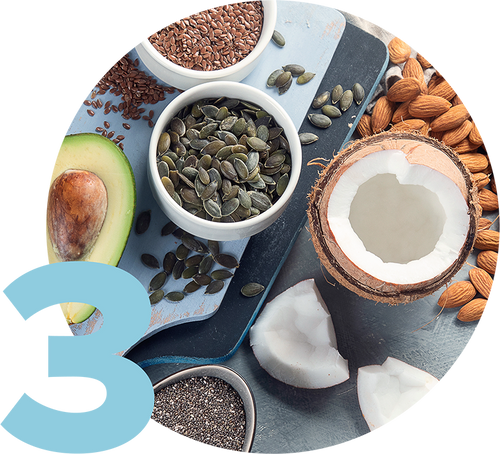 A variety of healthy foods including a halved avocado, bowls of pumpkin seeds and flaxseeds, a cracked coconut, almonds, and chia seeds arranged on a light blue surface. A large number 3 is in the bottom left corner.