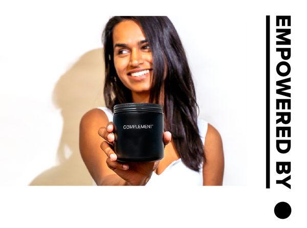 A person with long dark hair is smiling and holding a black jar labeled COMPLEMENT. The text EMPOWERED BY appears vertically on the right side of the image.