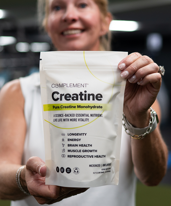 A smiling woman holds up a Complement-branded bag of Pure Creatine Monohydrate supplement, highlighting benefits like longevity, energy, brain health, muscle growth, and reproductive health.