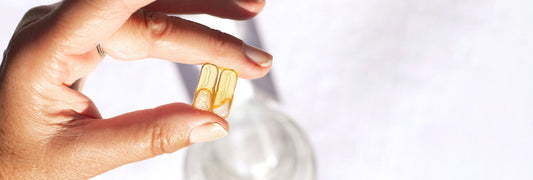 Female hand holding two supplement capsules, with a glass of water. 