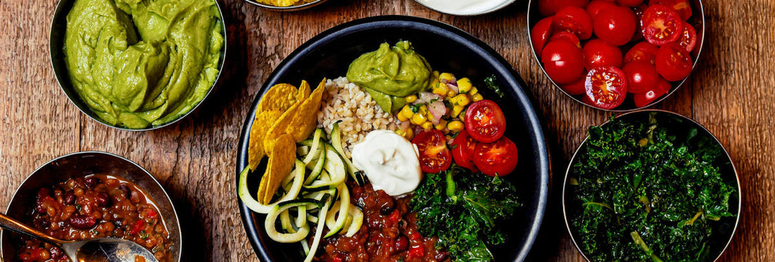 Bowl of food with rice and vegetables. Other bowls with guacamole, tomatoes, and kale next to it. 
