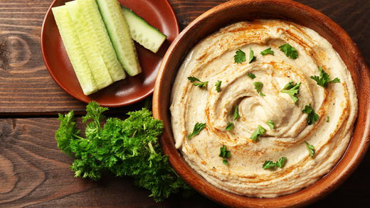 A bowl of hummus with celery sticks next to it.