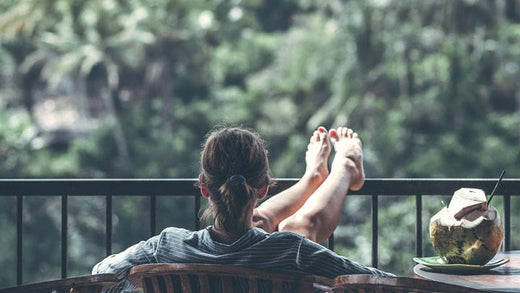 A woman relaxes on a balcony with a coconut next to her.