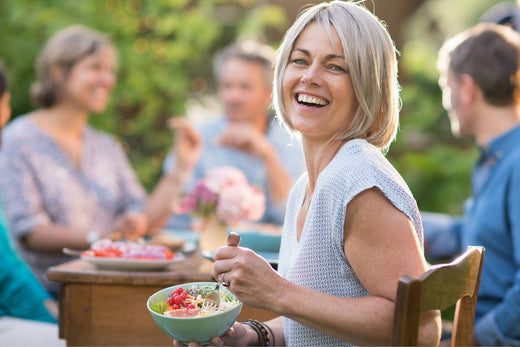 Woman sitting at a table eating a healthy salad while smiling