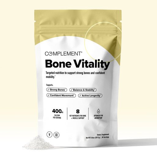 A beige and white pouch labeled COMPLEMENT Bone Vitality stands upright, with some powder spilled in front. The packaging highlights benefits like strong bones and 400 mg calcium per serving.