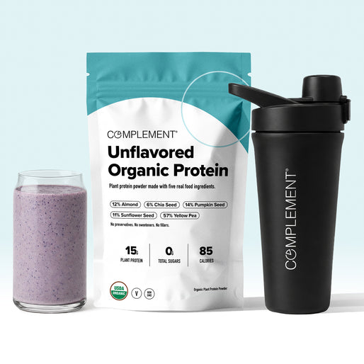 A glass of purple smoothie, a bag of Complement Unflavored Organic Protein powder, and a black Complement shaker bottle are displayed against a light background.