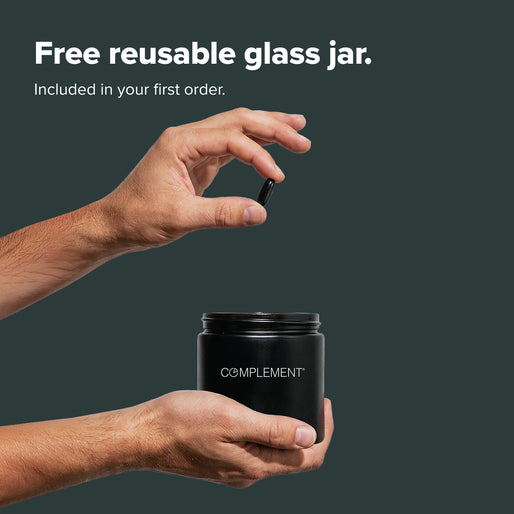 Two hands place a capsule into a black jar labeled Complement against a dark background. Text above reads, Free reusable glass jar. Included in your first order.