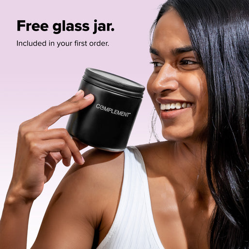 A smiling woman holds a black glass jar labeled Complement. Text above reads, Free glass jar. Included in your first order. The background is a soft gradient from pink to white.