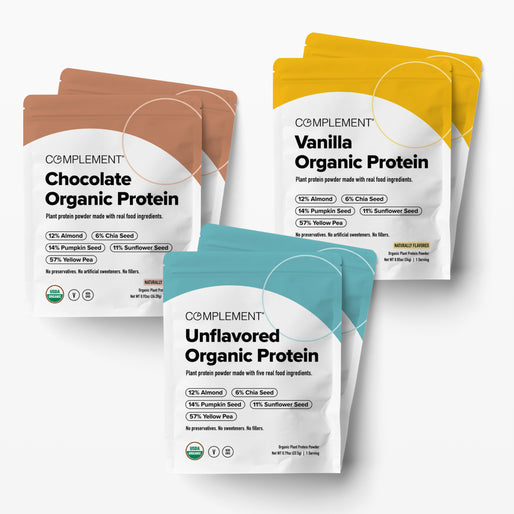 Four Complement organic protein powder packs in chocolate, vanilla, and unflavored varieties, labeled with ingredients like almond, chia, pumpkin, and sunflower seed, arranged on a white background.