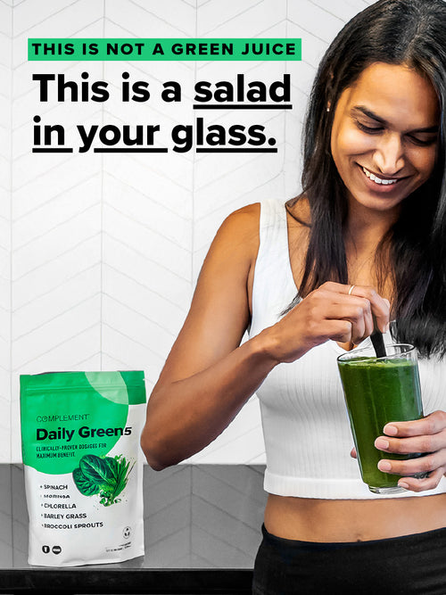 A person in a white tank top stirs a green drink in a glass with a spoon, near a packet of Complements Daily Greens, loaded with superfoods like spinach and spirulina to enhance immunity and brain health. Text states: This isnt just green juice; its a salad in your glass.