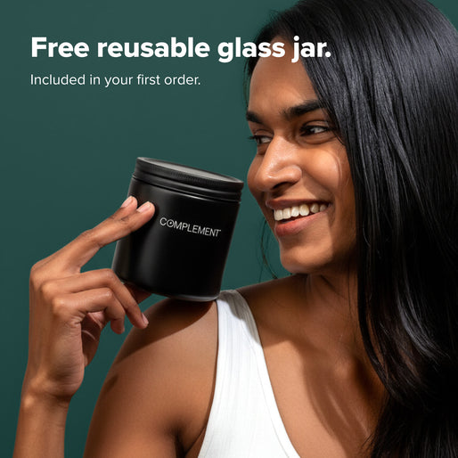 A smiling woman in a white top holds a black jar labeled COMPLEMENT near her face. Text above reads, Free reusable glass jar. Included in your first order, against a green background.