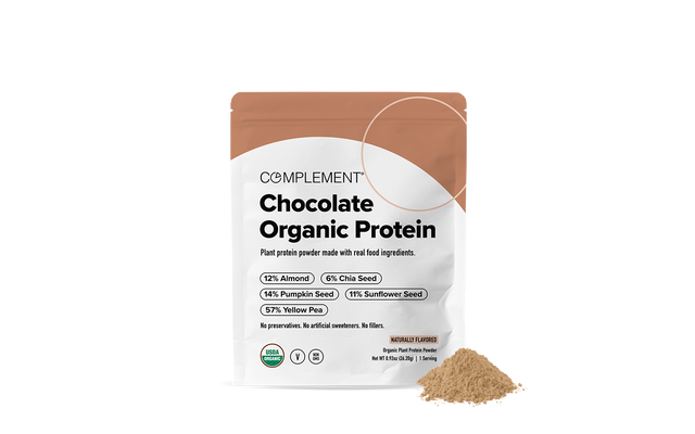 A pouch of Complement Chocolate Organic Protein powder stands upright, with a small mound of light brown powder to its right. The packaging lists protein sources and highlights its organic and plant-based ingredients.