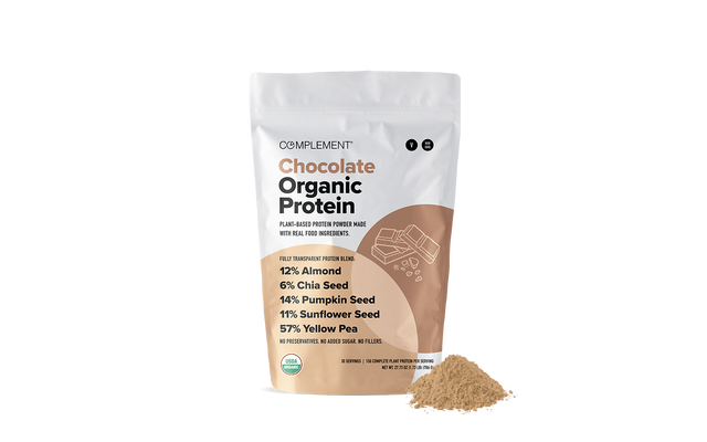 A bag of Complement Chocolate Organic Protein powder stands upright with a small pile of the powder in front. The bag lists ingredients and nutritional percentages, and features a minimalist brown and white design.