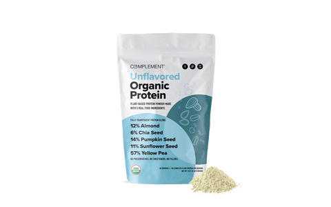 A bag of Complement Unflavored Organic Protein powder stands upright, with a small heap of the light-colored powder beside it. The packaging lists ingredients and percentages, including almond, chia seed, pumpkin seed, sunflower seed, and yellow pea.