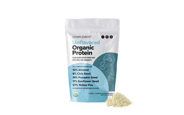 A bag of Complement Unflavored Organic Protein powder stands upright, with a small heap of the light-colored powder beside it. The packaging lists ingredients and percentages, including almond, chia seed, pumpkin seed, sunflower seed, and yellow pea.