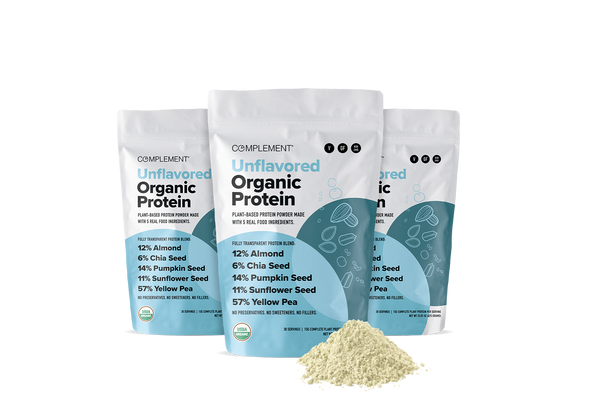 Three white pouches labeled Complement Unflavored Organic Protein stand upright, with light blue accents. In front, theres a small pile of pale protein powder. The pouches highlight the plant-based ingredients.