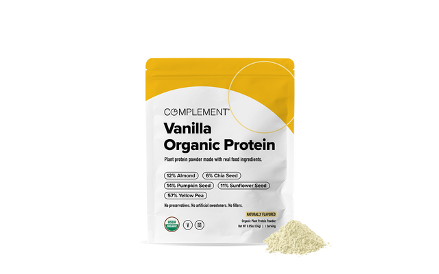 A standing pouch of Complement Vanilla Organic Protein powder with a small pile of powder in front. The packaging lists ingredients like almond, chia seed, pumpkin seed, sunflower seed, and yellow pea.