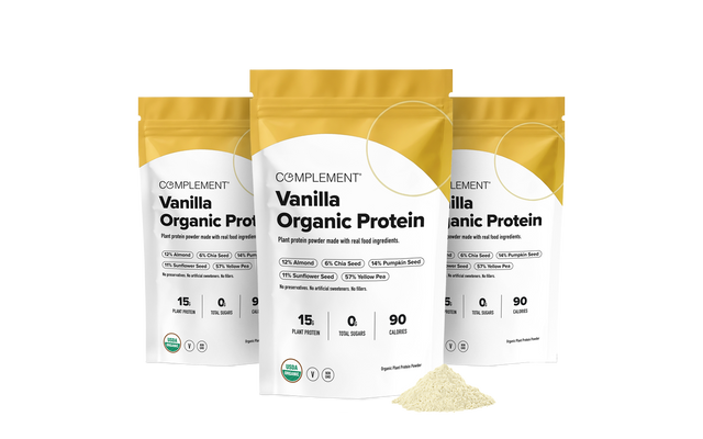 Three pouches of Complement vanilla organic protein powder, with a small pile of powder in the foreground.