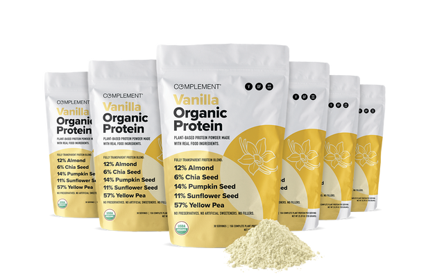 Six bags of Complement Vanilla Organic Protein powder are arranged in a row with a small pile of the light-colored powder in front. The packaging is white and yellow with ingredient percentages listed.