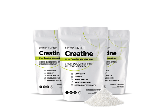 Three standing pouches of Complement Creatine Monohydrate supplement with white and green packaging, alongside a small mound of white creatine powder in front. The packaging highlights benefits like longevity, energy, and muscle growth.