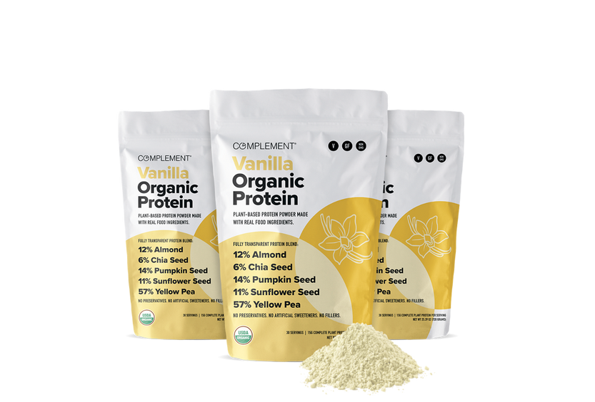 Three white and yellow bags of Complement Vanilla Organic Protein powder are displayed, with organic certification and key ingredients listed. A small pile of the powder is in front of the bags.