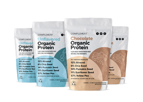 Four bags of Complement Organic Protein powder are displayed. They include Unflavored (blue), Chocolate (brown), and Vanilla (beige) flavors. Each bag lists ingredients like almond, chia seed, pumpkin seed, sunflower seed, and yellow pea.