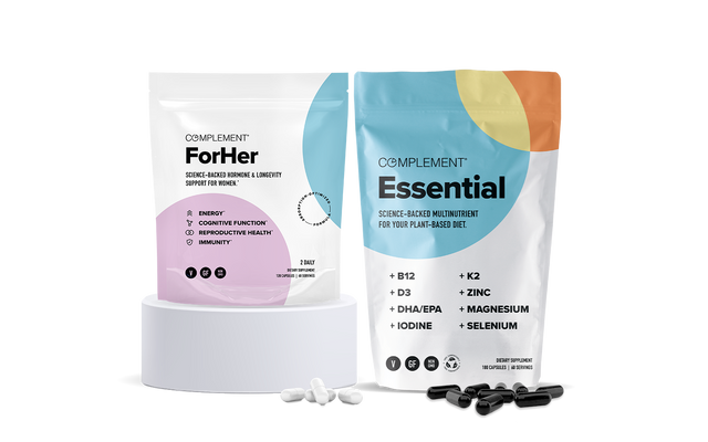 Two supplement packages on a white background: ForHer in a white-pink pouch, and Essential in a colorful pouch. White and black capsules are scattered in front of their respective packages on a round white platform.