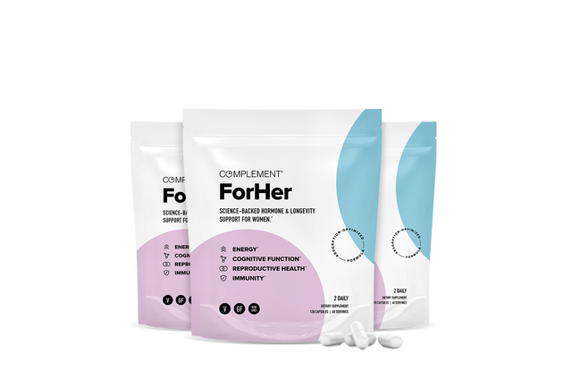 Three white and pastel-colored supplement pouches labeled Complement ForHer with scattered white capsules in front. The packaging highlights benefits: energy, cognitive function, reproductive health, and immunity.