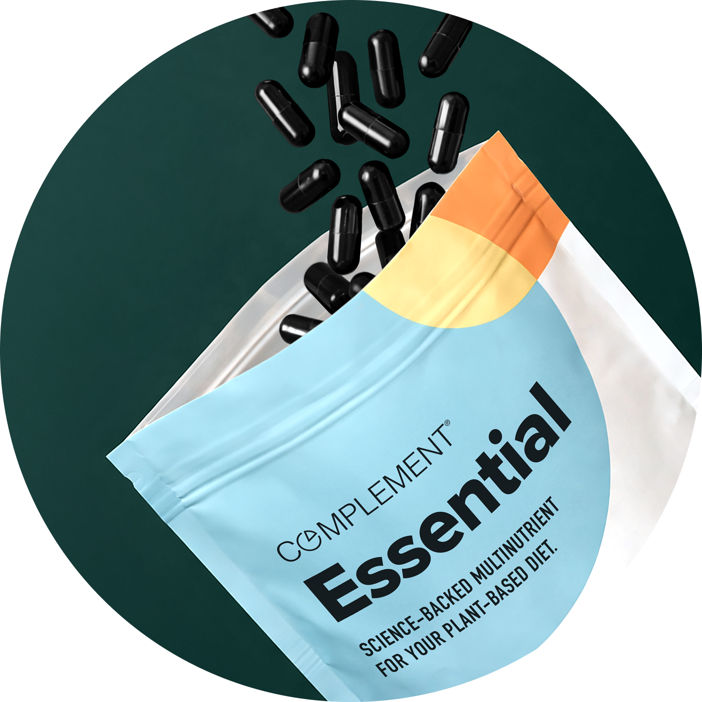 A white and light blue pouch labeled Complement Essential spills black capsules onto a dark green surface. The text on the pouch reads: Science-backed multinutrient for your plant-based diet.
