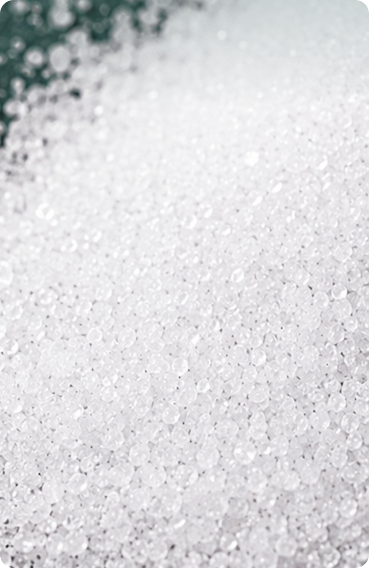 A close-up image of numerous small, round, clear or white granules spread across a surface, creating a textured, crystalline appearance.